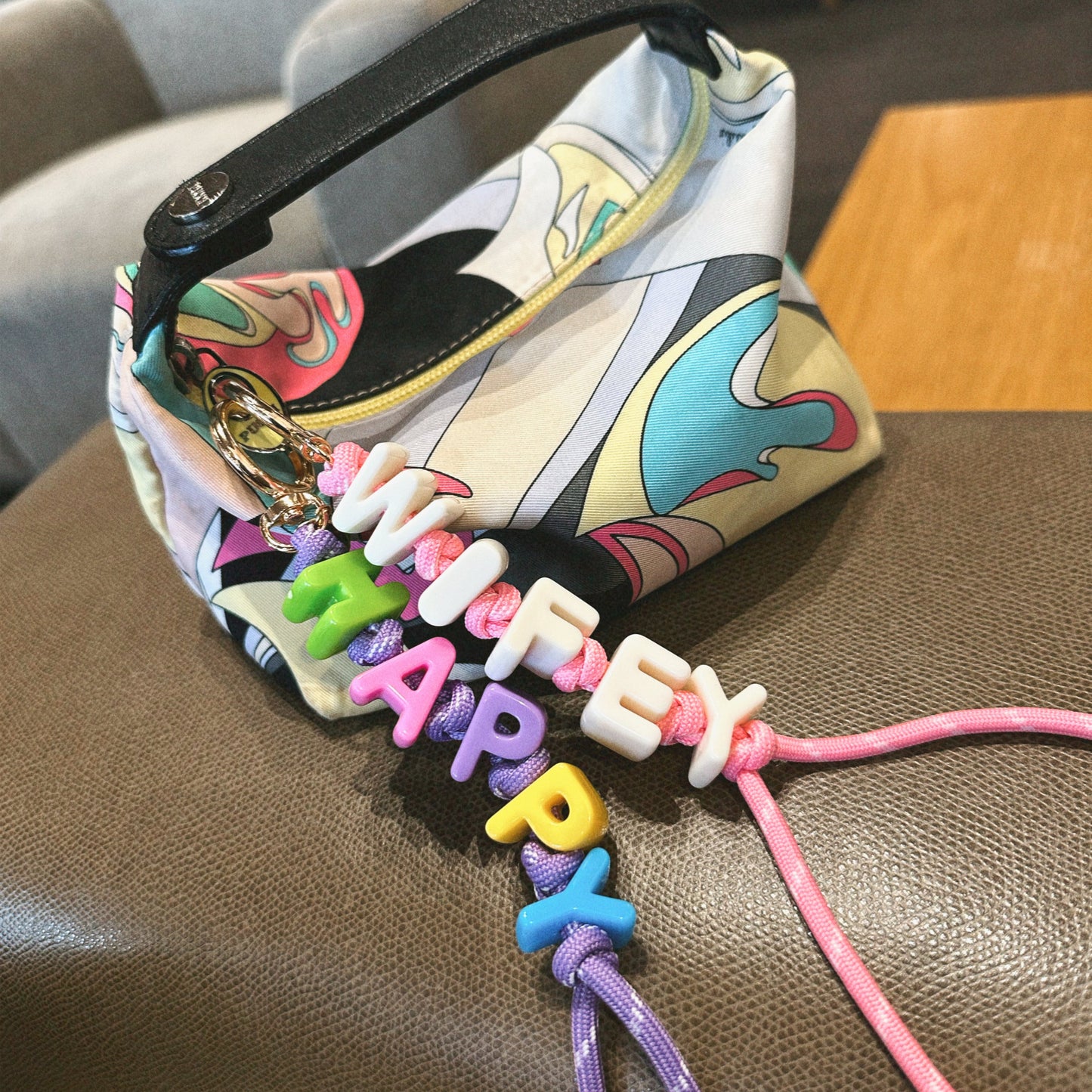 Colorful keychain with 'HAPPY' letters attached to a patterned bag on a brown surface.