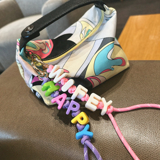 Colorful keychain with 'HAPPY' letters attached to a patterned bag on a brown surface.