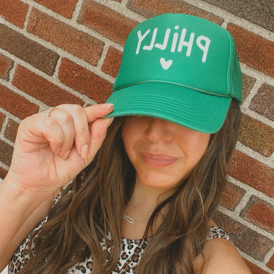Person wearing a green cap with 'PHILLY' text against a brick wall